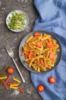 Tortiglioni semolina pasta with tomato and microgreen sprouts on a black concrete background and