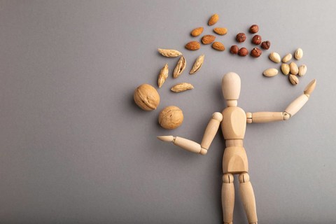 Wooden mannequin juggling nuts on gray pastel background. close up, isolated, delivery concept,
