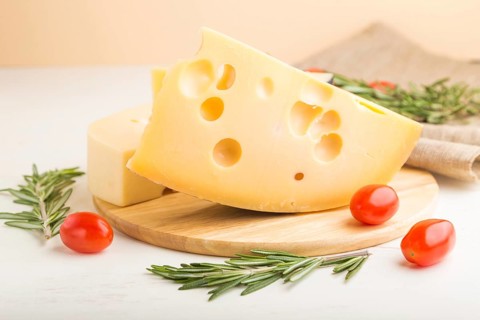 Various types of cheese with rosemary and tomatoes on wooden board on a white wooden background and