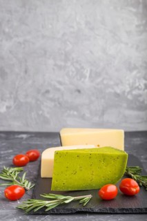 Green basil cheese and various types of cheese with rosemary and tomatoes on black slate board on a