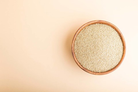 Wooden bowl with raw white quinoa seeds on a pastel orange background. Top view, flat lay, copy