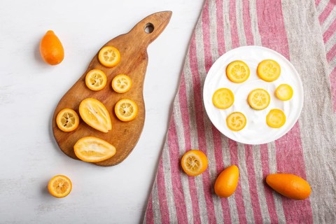 Greek yogurt with kumquat pieces in a white plate on a white wooden background, copy space