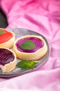 Sweet tartlets with jelly and milk cream with cup of coffee on a black concrete background and pink