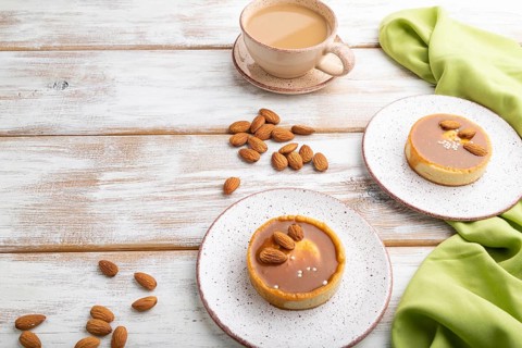 Sweet tartlets with almonds and caramel cream with cup of coffee on a white wooden background and