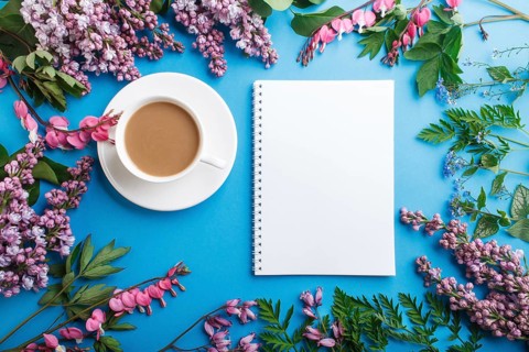 Purple lilac and bleeding heart flowers and a cup of coffee with notebook and colored pencils on