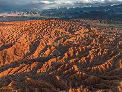 Landscape of eroded hills, badlands at sunset, mountain peaks of the Tian Shan Mountains in the