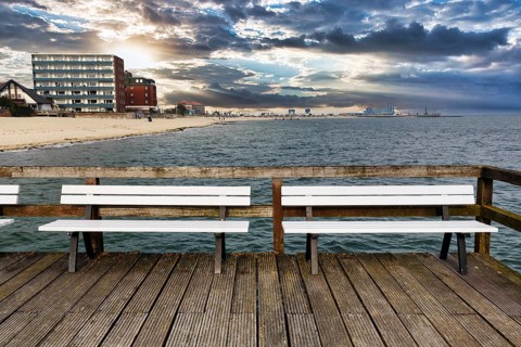 Empty benches on the pier with a view of the beach, houses and ferry port, autumn weather, Wyk auf