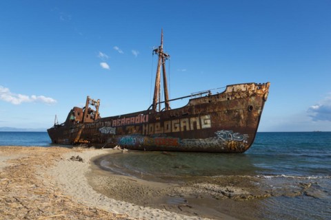 A rusty shipwreck with graffiti on a sunny beach under a blue sky with clouds, Dimitrios shipwreck,