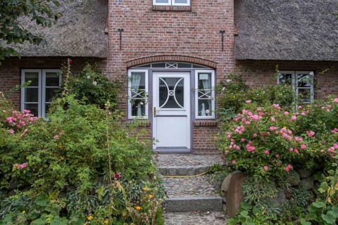 A charming thatched brick house with blooming roses and lush greenery on a sunny day, North Sea