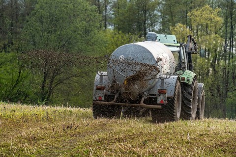 Slurry is spread on a field with a tractor from a slurry tanker to fertilise the farmland, North