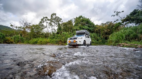 Toyota off-road vehicle with roof tent drives through a wide river in the rainforest, Alajuela