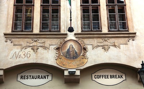 Old historic façade with image of the Virgin Mary and signs for restaurant and coffee break in the
