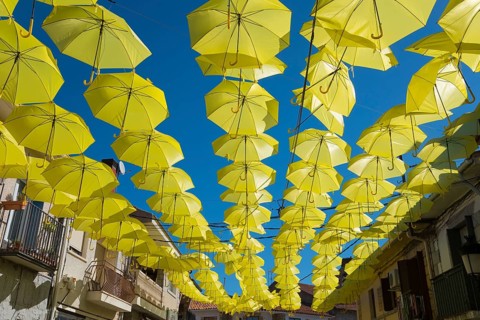 Artistic installation of yellow umbrellas over a street, enveloped by balconies and old buildings