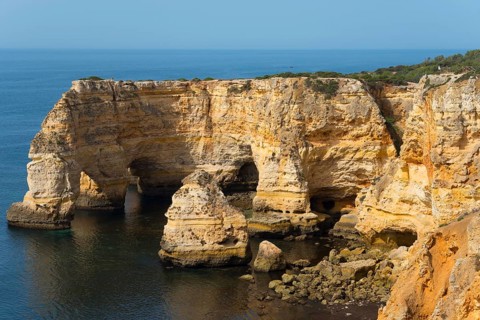 Steep cliffs and craggy rocks jut out of the calm sea on a clear day, Praia da Marinha, Lagoa,