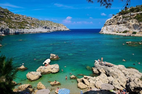 An idyllic bay with crystal-clear water, surrounded by rocks under a bright blue sky, Anthony Quinn