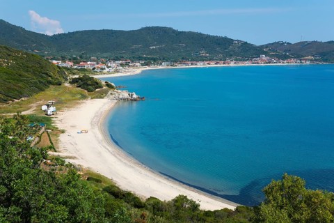 View of a quiet coastal landscape with beach and azure blue sea, surrounded by hills and small