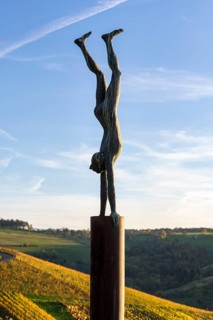 A statue of a person doing a handstand on a metal post in front of a landscape background at