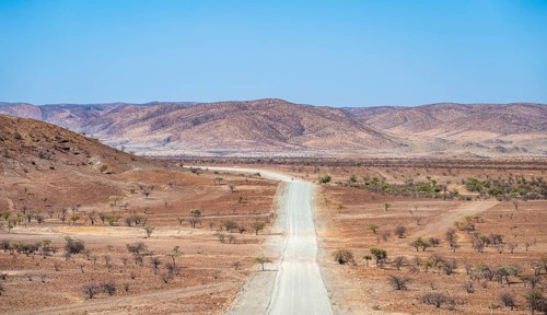 Gravel track leads through barren dry landscape with red and yellow hills, Kaokoveld, Kunene,