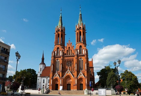 Red brick church with two towers and outbuildings under a cloudy sky, Church of the Blessed Virgin