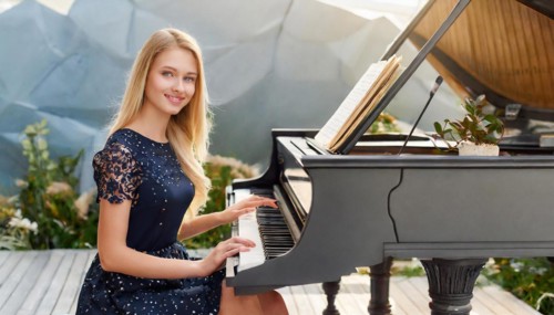 A young woman in a blue dress smilingly plays a black grand piano in a modern room, AI generated,