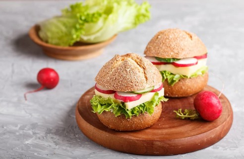 Sandwiches with cheese, radish, lettuce and cucumber on wooden board on a gray concrete background.