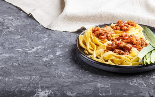 Tagliatelle bolognese pasta with minced meat on a black concrete background. side view, close up,