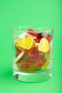 Various fruit jelly candies in drinking glass on green pastel background. side view, close up