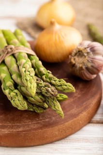 Bunch of fresh green asparagus, garlic, onion on white wooden background. Side view, selective