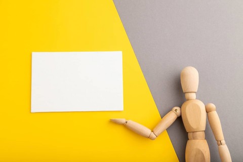 Wooden mannequin holding white blank poster on gray and yellow pastel background. copy space,