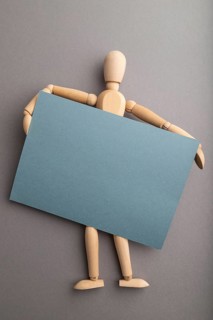 Wooden mannequin holding blue blank poster on gray pastel background. copy space, isolated,