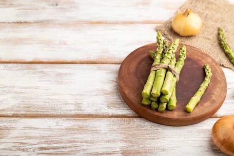 Bunch of fresh green asparagus, garlic, onion on white wooden background. Side view, copy space.