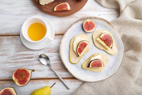 Summer appetizer with pear, cottage cheese, figs and honey on a white wooden background and linen