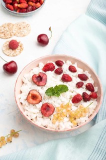 Rice flakes porridge with milk and strawberry in ceramic bowl on white concrete background and blue