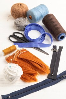 Sewing accessories: scissors, thread, thimbles, braid on white wooden background. Side view, close