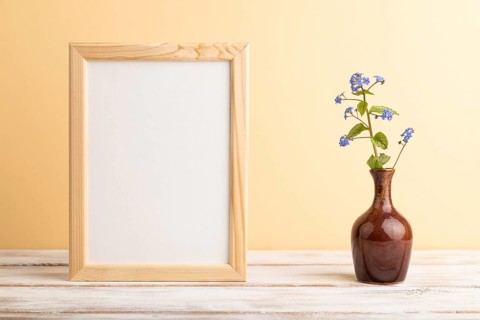 Wooden frame with blue forget-me-not flowers in ceramic vase on orange pastel background. side