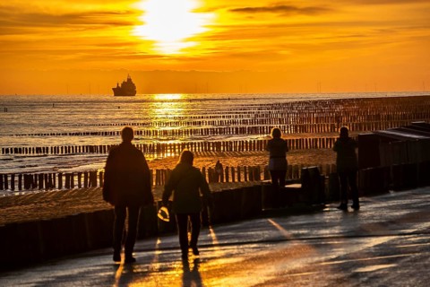 Sunset on the beach of Zoutelande, beach with wooden pile breakwaters, tourists, cargo ship sailing