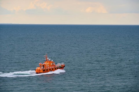 An orange pilot boat sailing on the open sea under a cloudy sky, Kiel, Schleswig-Holstein, North