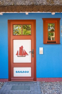 Colourful front door in brown, white and blue with a sailing ship as a motif and matching window