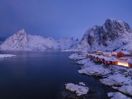 Rorbuer huts of Hamnoy at the fjord at dusk, snowy mountains in the background, Hamnøy, Reine,