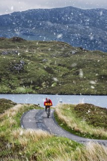 Lonely biker cycling through the Scottish Highlands on heavily laden touring bicycle along single