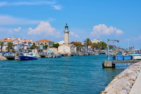 Coastal town with colourful houses and palm trees, boats in the water and a lighthouse, on a sunny