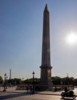 Sunbeams behind an obelisk, Eiffel Tower in the background, a motorbike passing by, Paris