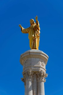 Golden statue of Jesus on a high column in front of a blue sky, Christ statue, Santuario de Fatima,