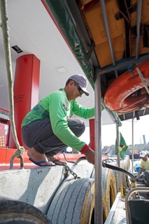Brazilian man refuelling a boat from a floating petrol station on the Rio Negro, Manaus, Amazonas