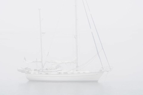 Sailboat, sailing boat, yacht with lowered sails anchored at sea during bad visibility due to thick