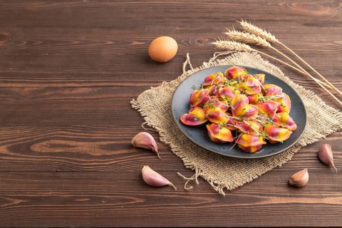 Rainbow colored dumplings with pepper, herbs, microgreen on brown wooden background and linen
