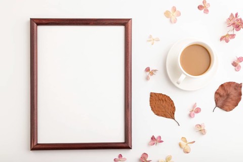 Composition with wooden frame, brown beech autumn leaves, hydrangea flowers and cup of coffee.