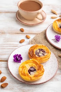 Small cheesecakes with jam and almonds with cup of coffee on a white wooden background and linen