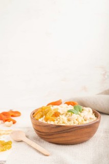 Bulgur porridge with dried apricots, raisins and cashew in wooden bowl on a white wooden background