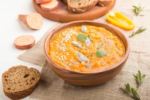 Sweet potato or batata cream soup with sesame seeds in a wooden bowl on a white wooden background